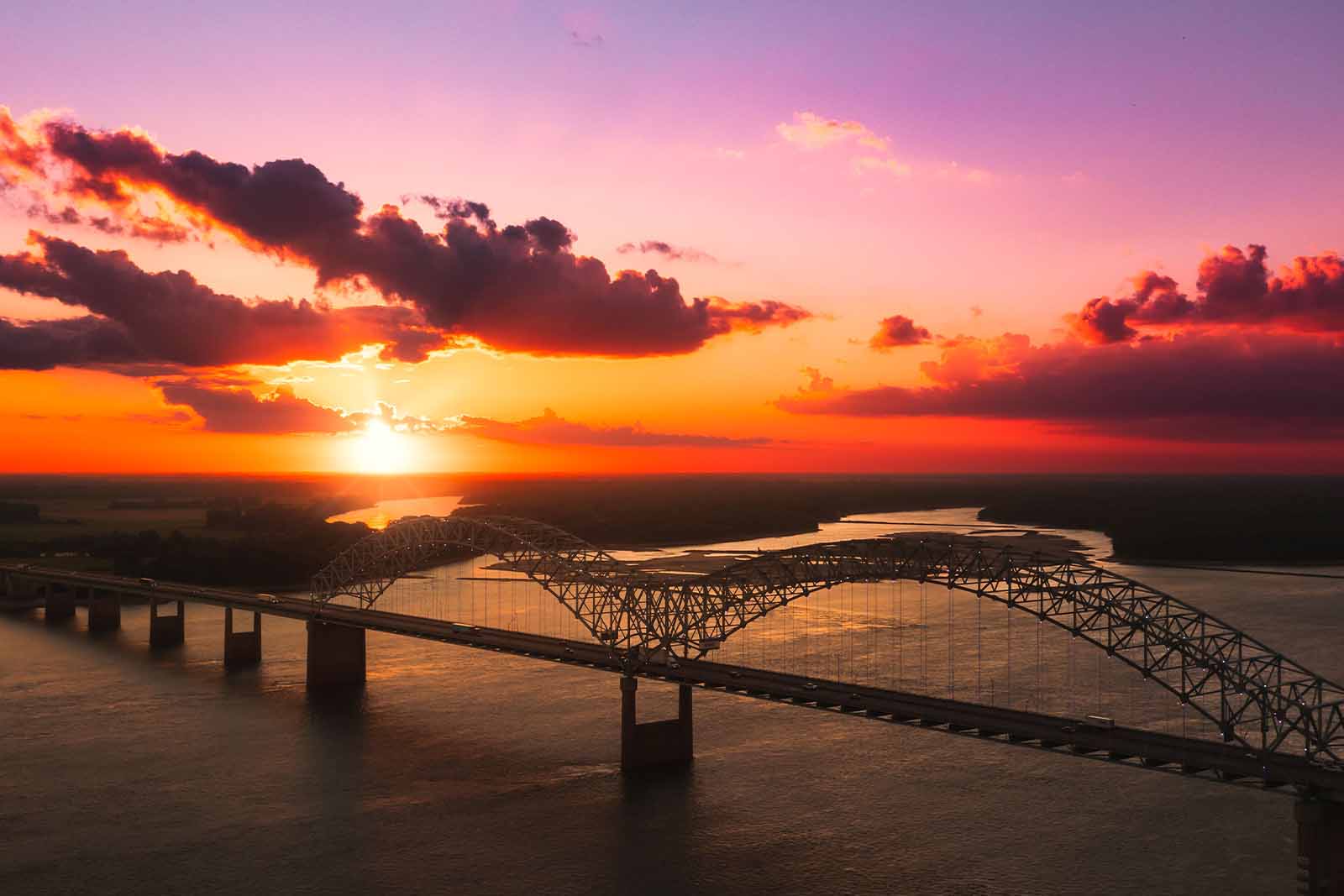 Imagem de uma ponte que atravessa um mar, vista de cima sob o nascer do sol 