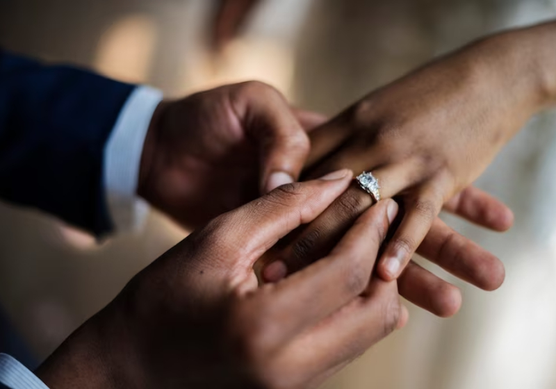 imagem de um homem colando aliança de casamento no dedo de uma mulher 