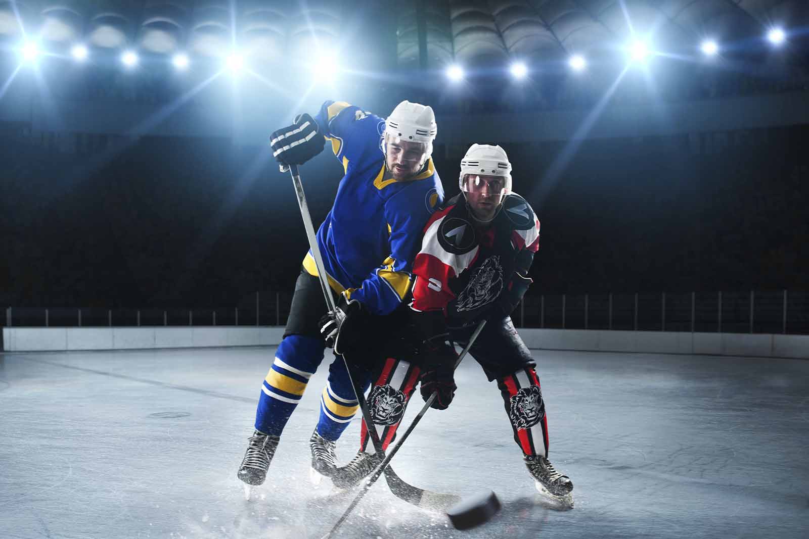 Imagem de dois jogadores de Hóquei no gelo de times diferentes disputando pelo disco em uma arena de hóquei no gelo 