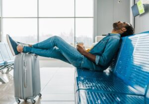 Homem sentado em um banco escorando as pernas em sua mala de viagem