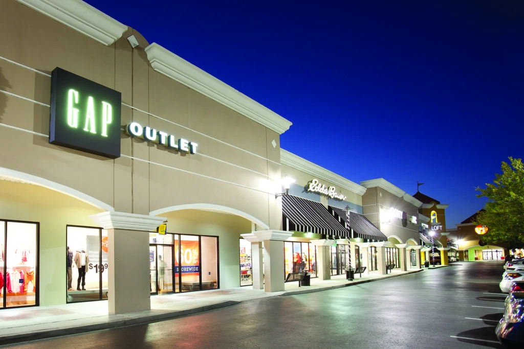 Vista noturna de um centro de compras outlet com lojas como Gap e Eddie Bauer, um destino popular para turistas e viajantes em busca de ofertas e lazer em seu roteiro.