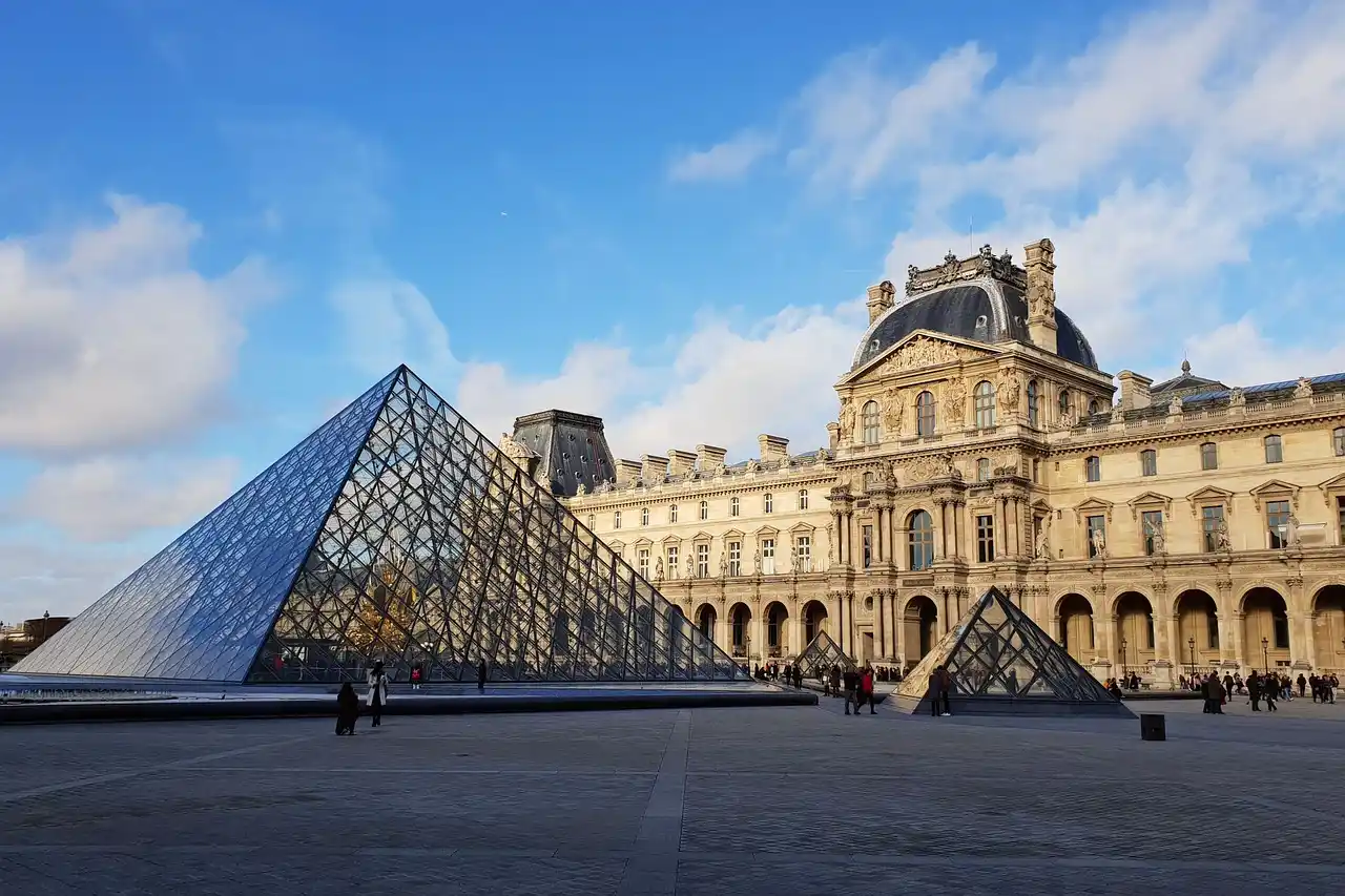 A famosa Pirâmide de Vidro do Louvre e o grandioso edifício histórico do museu em Paris, um destino turístico essencial para informações sobre viagens na França.