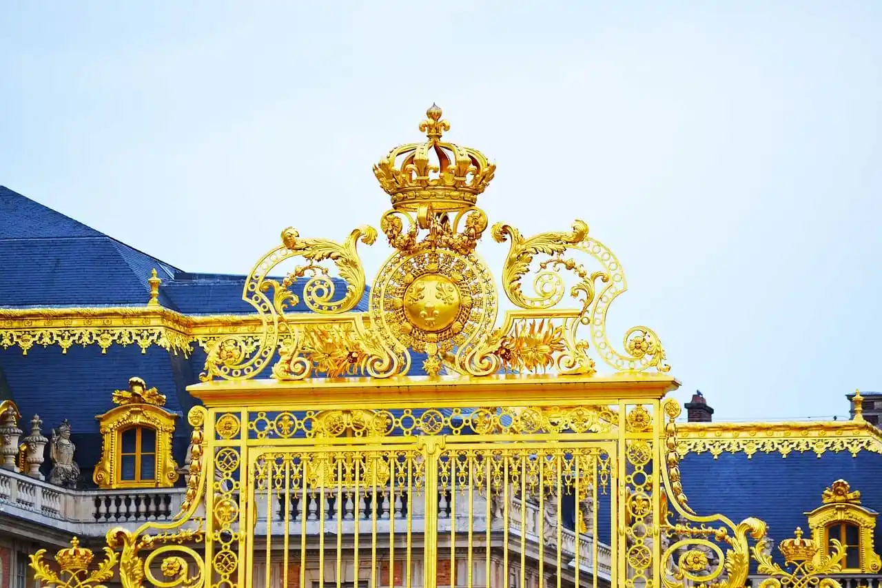 Portão dourado ornamentado com coroa e flor-de-lis do Palácio de Versalhes, França. Um destino de viagem histórico e luxuoso.