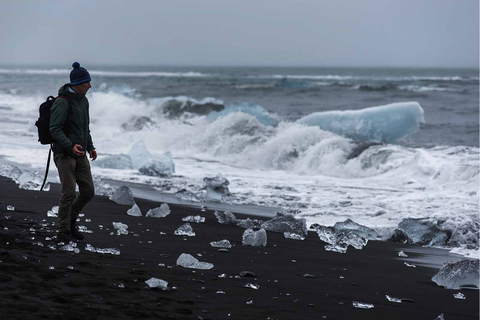 Imagem de um turista com roupas de frio e mochila, na beira da orla na islândia de tarde 