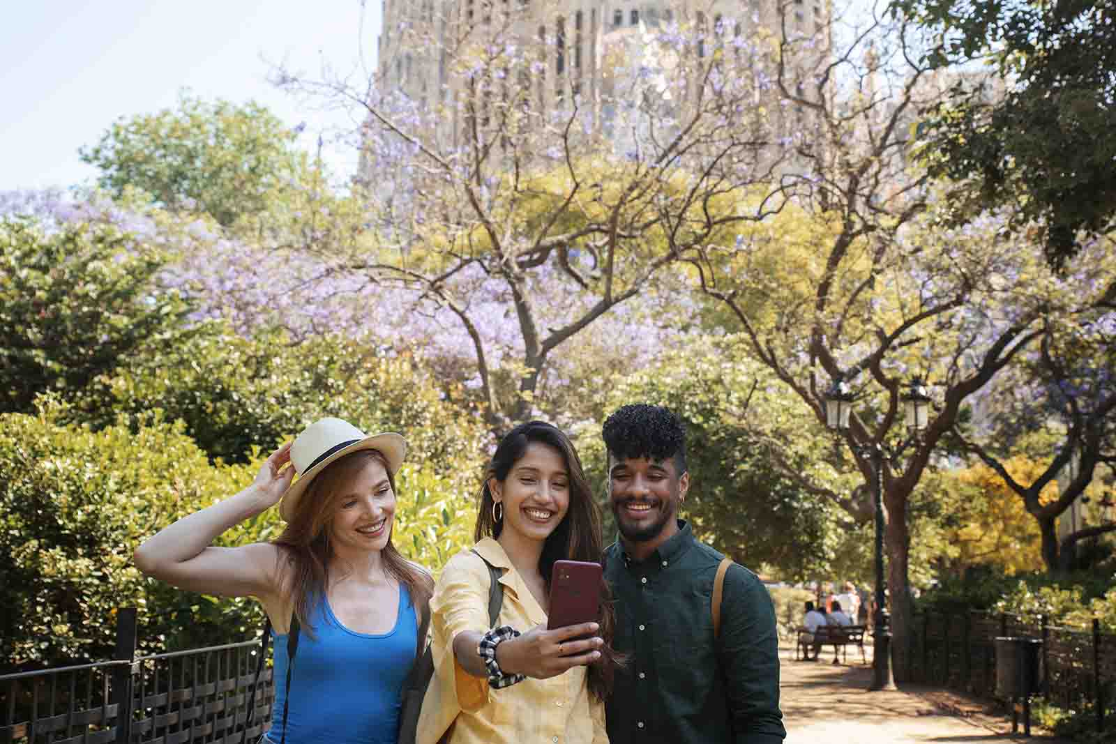 Imagem de três amigos tirando um selfie em um parque com diversas árvores de dia 
