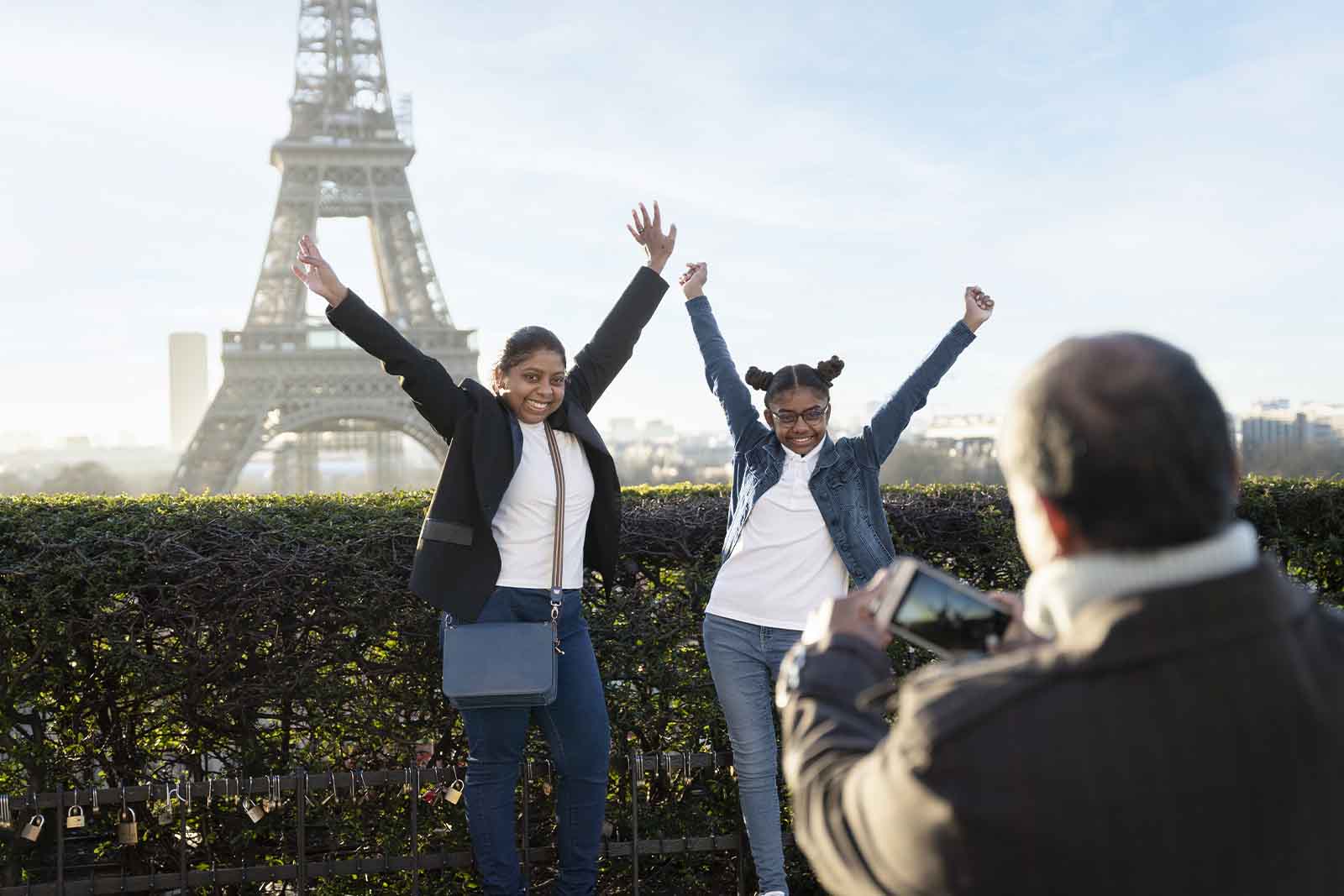 Imagem de uma família tirando uma foto com a torre de paris de fundo, de dia 