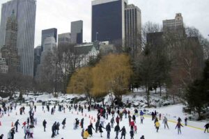 Imagem de diversas pessoas patinando no gelo em um park em Nova Iorque, de dia e no inverno