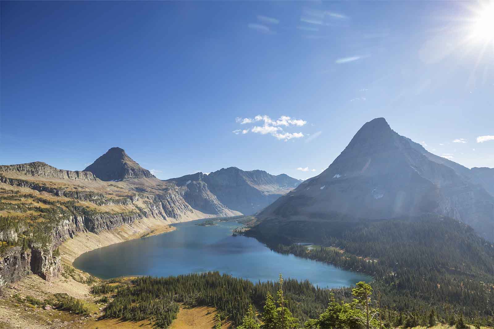 Imagem do Glacier National Park de dia, com diversas montanhas, um grande lago e larga floresta