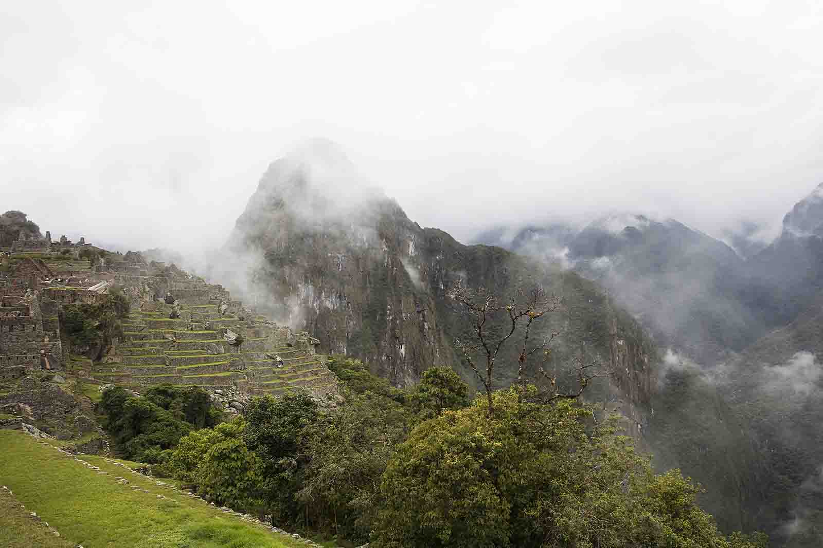 Imagem de Machu Pichu no Peru, com uma vasta área com árvores, grama, montanhas, nuvens e de dia 