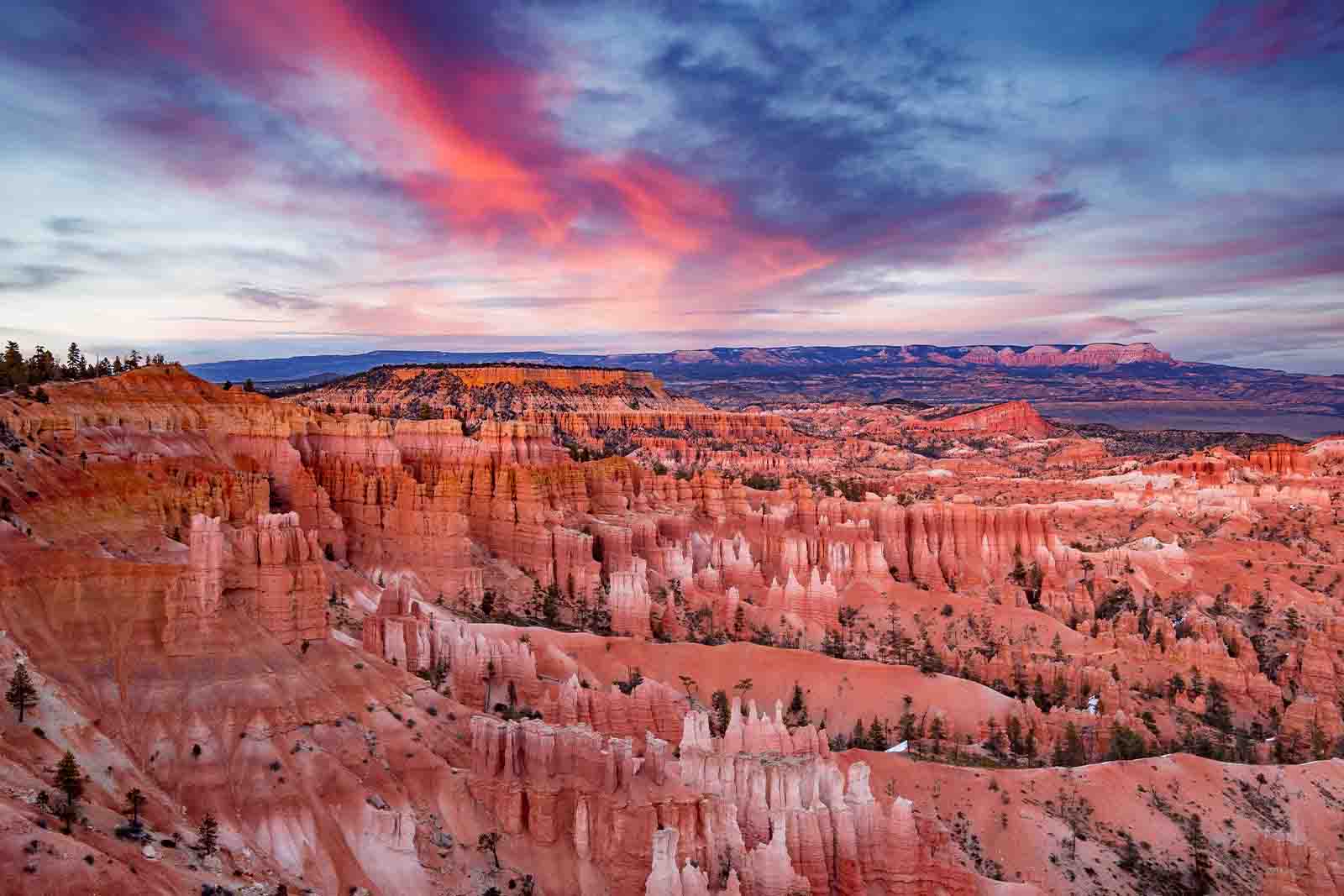 Imagem do Bryce Canyon National Park durante o por do sol, com diversas montanhas de cor laranja e o céu azul com tons laranjas 