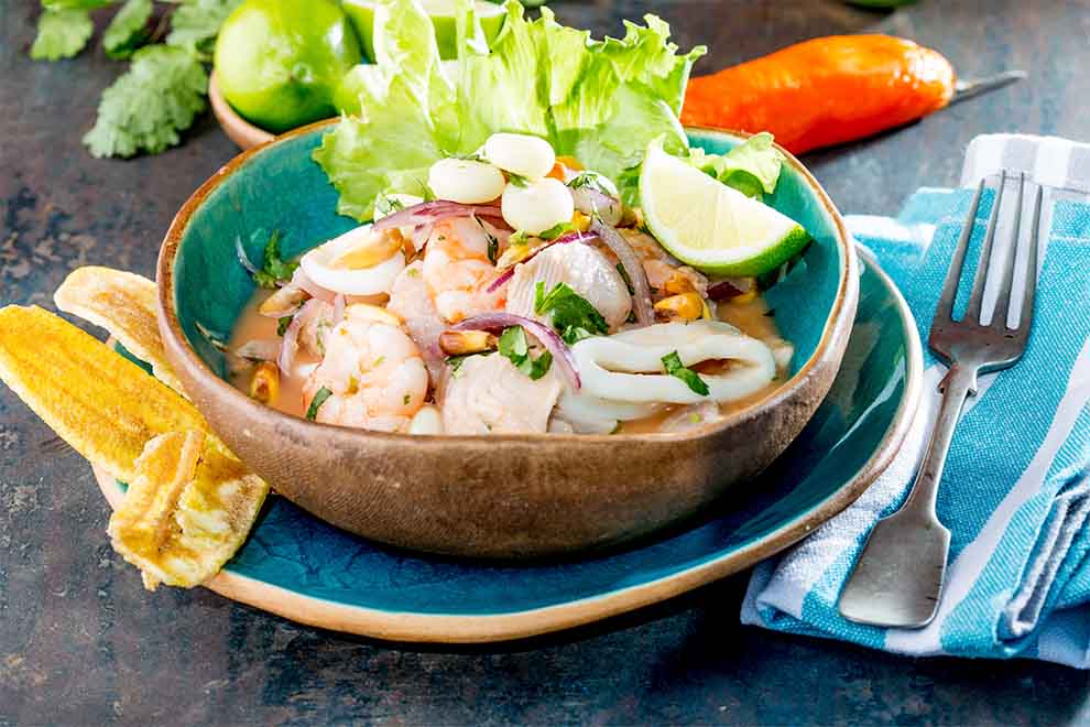 ceviche dentro de um pequeno bowl de ceramica em cima de um pequeno prato de porcelana e com talheres ao lado em cima de um pano listrado em azul e branco