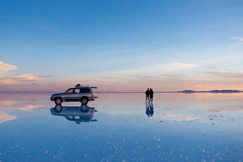 Salar de Uyuni com um carro junto de um casal no por do sol na Bolívia 