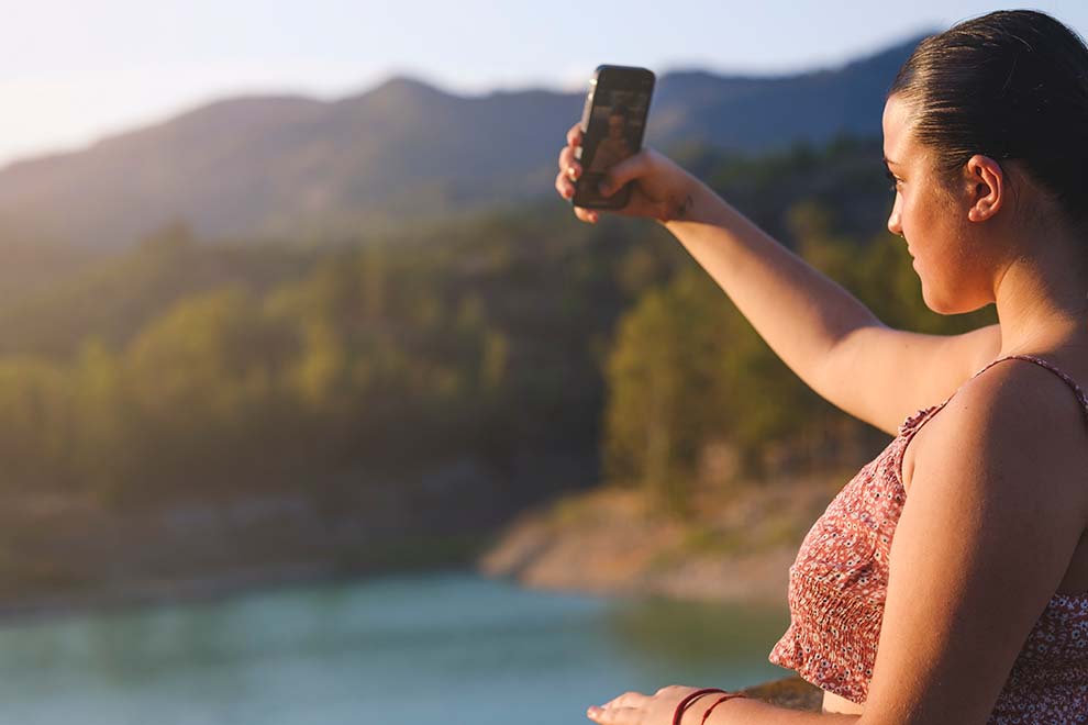 Mulher tirando selfie com fundo natural ao pôr do sol