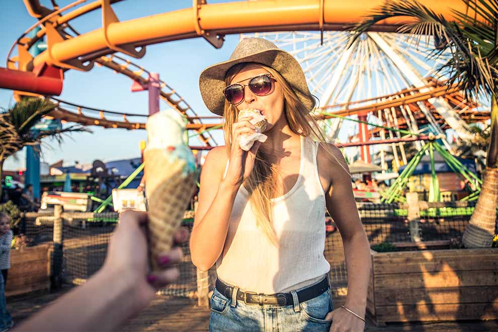 Mulher se deliciando com sorvete em parque de diversões.