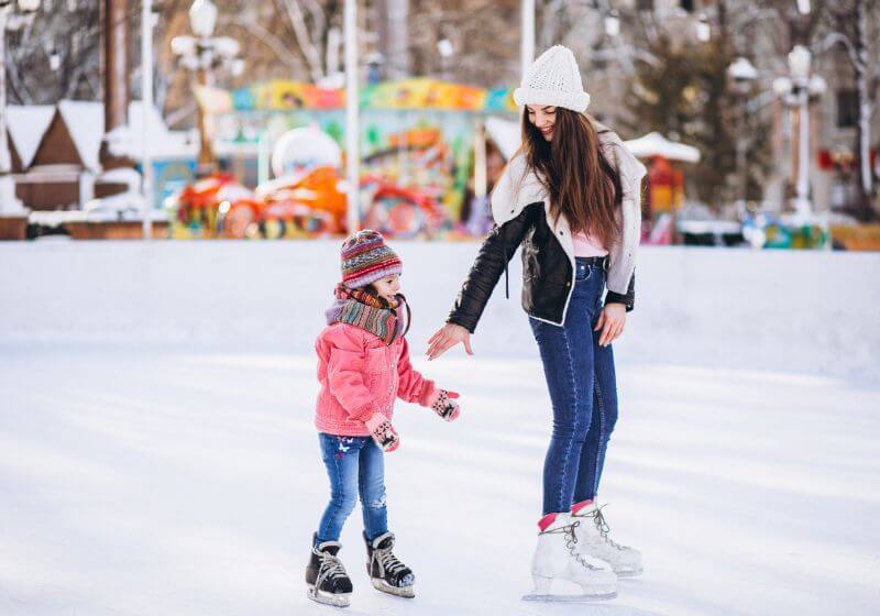 Mãe e filha patinando no gelo em parque de inverno