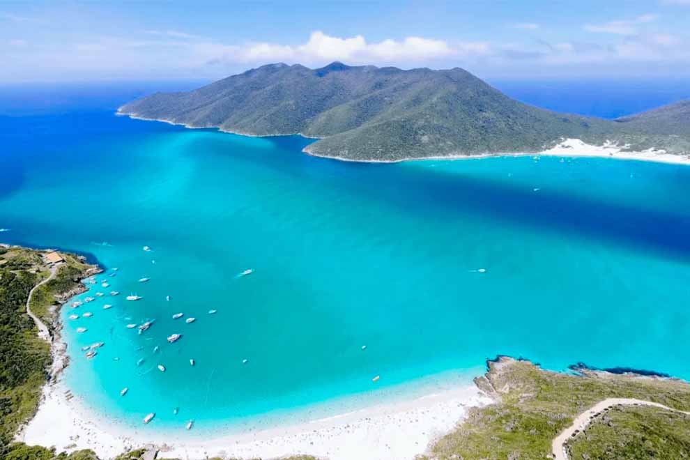 Vista aérea da praia com água cristalina e montanhas ao fundo