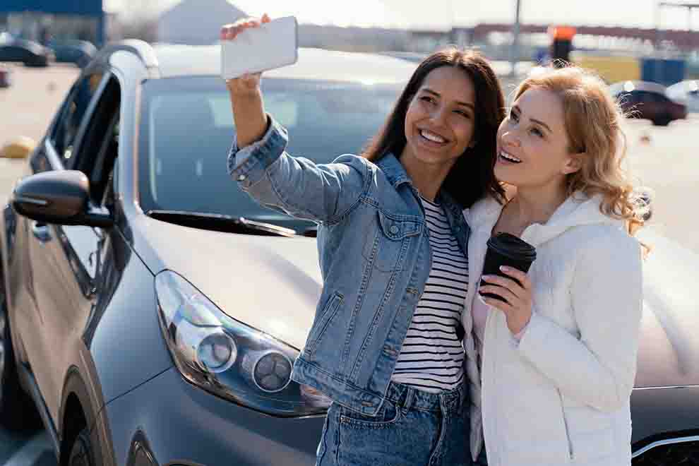 Duas amigas tirando selfie ao lado de carro