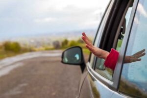 Criança com braço de fora de carro em passeio.