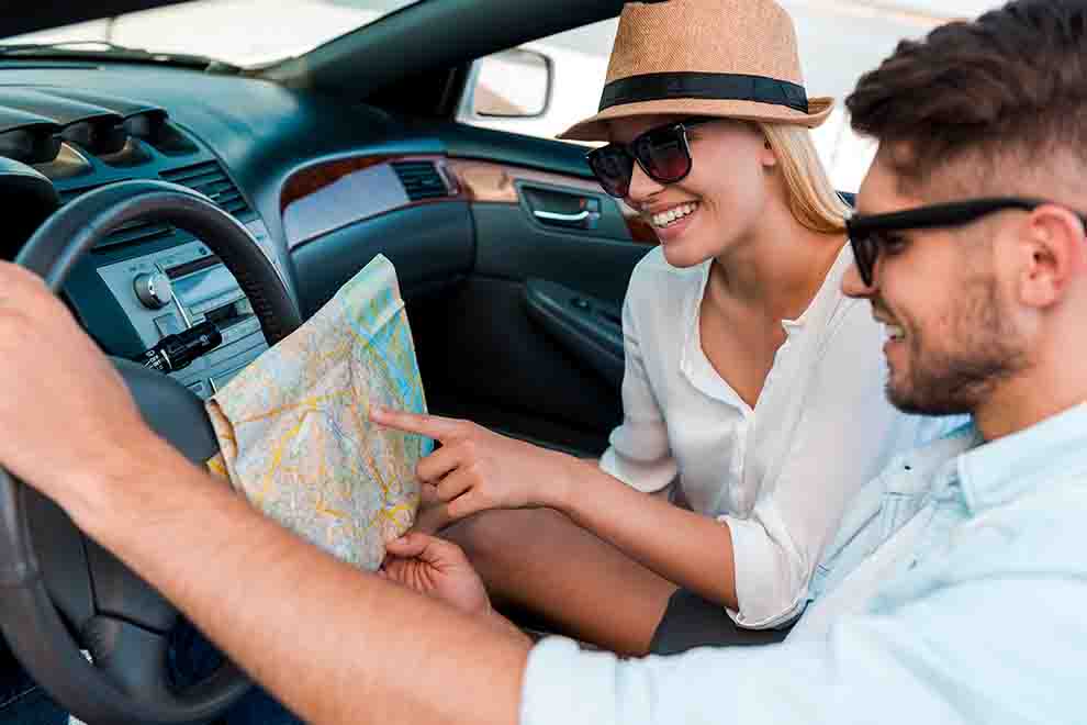 Casal sorridente analisando um mapa dentro do carro.