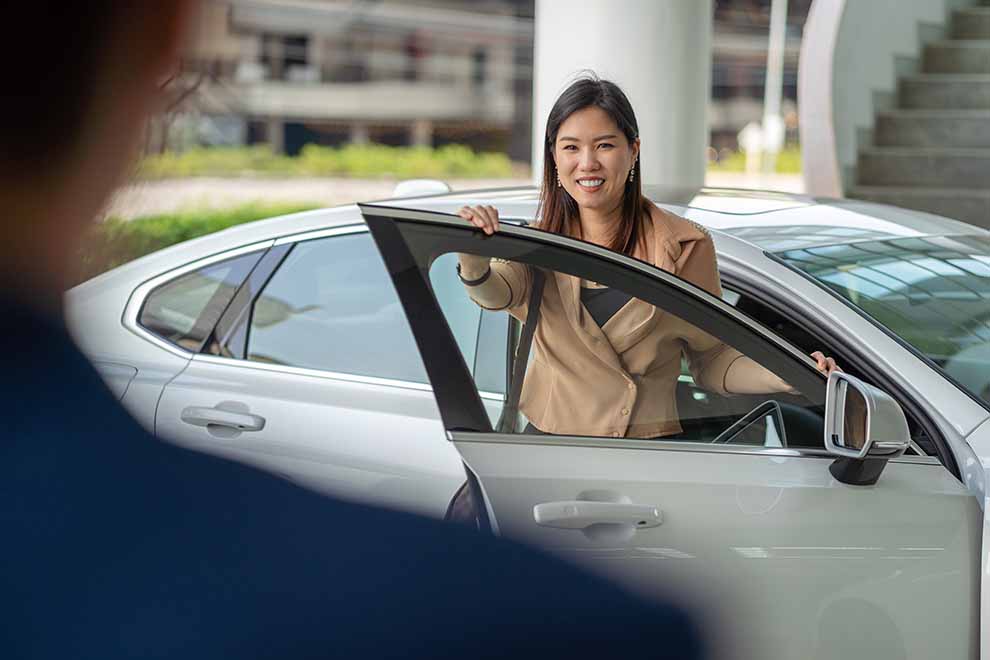 Mulher sorrindo ao lado de carro em estacionamento