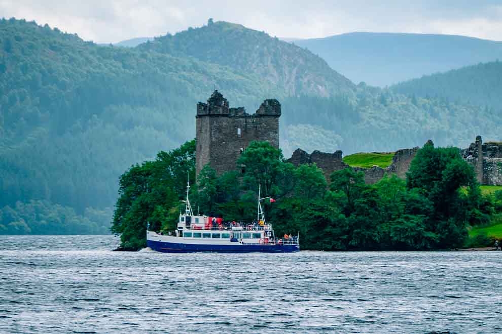 Barco no lago com castelo e montanhas ao fundo