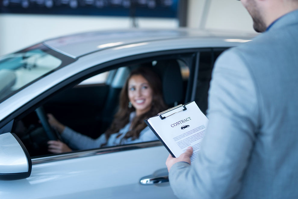 Cliente sorridente em carro enquanto assina contrato.