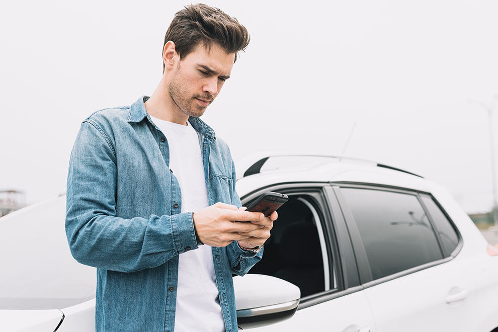 Homem usando smartphone ao lado de carro branco.