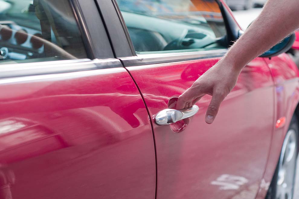 Homem abrindo a porta de um carro vermelho.